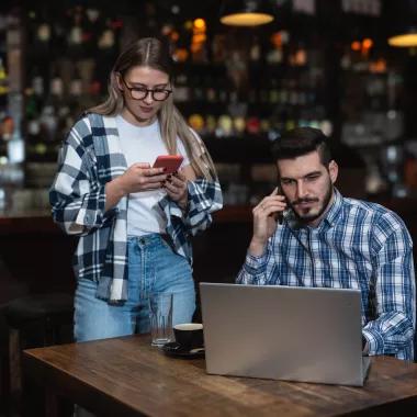 Man making a phonecall at a pub with a woman looking at her phone beside him